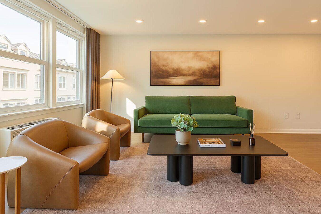 En moderne stue med en grøn sofa, to læderlænestole, et sofabord og en gulvlampe.