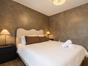 Une chambre à coucher avec un grand lit, deux tables de chevet et un luminaire fixé au mur.
