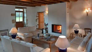 Una sala de estar acogedora con chimenea, vigas de madera, muebles blancos y una pared de piedra.