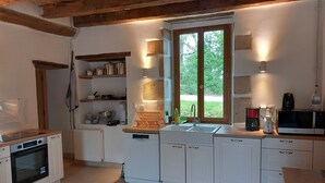Una cocina moderna con armarios blancos, horno empotrado, lavavajillas y un amplio ventanal con vistas al verdor.