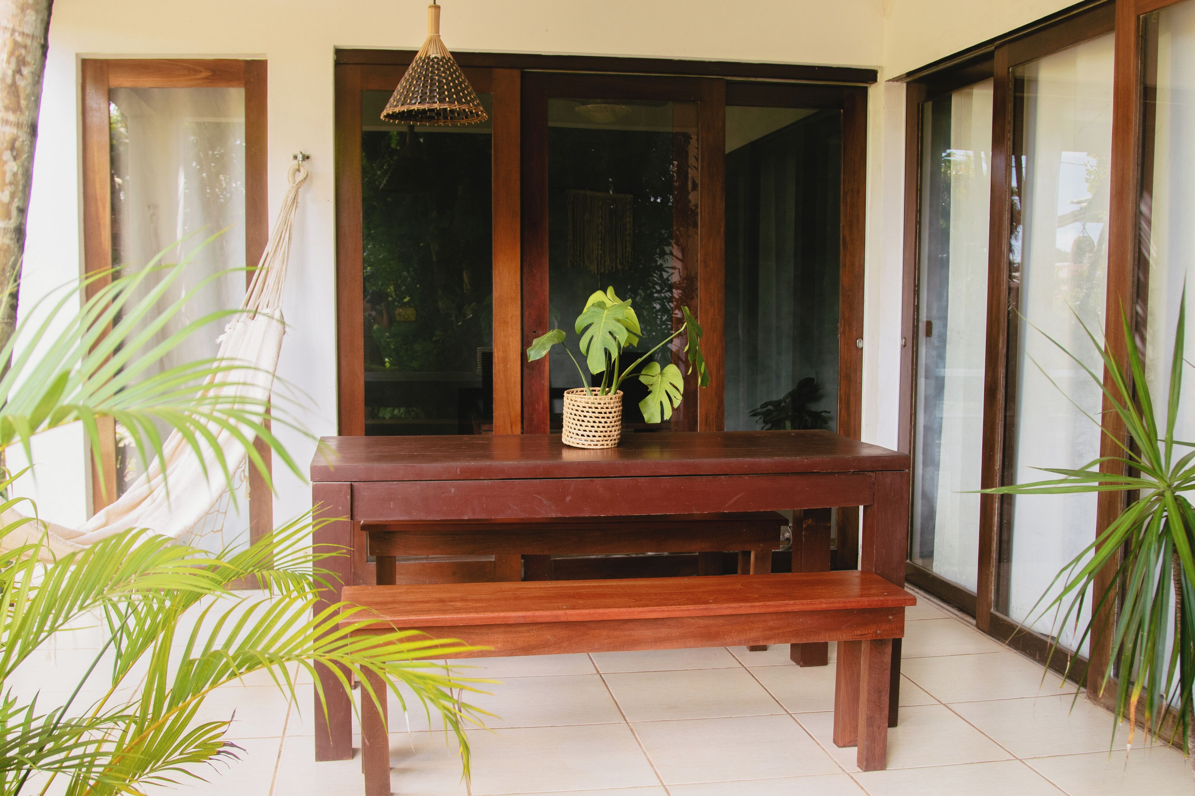 Una mesa de madera con un banco, una lámpara colgante y una planta en maceta.
