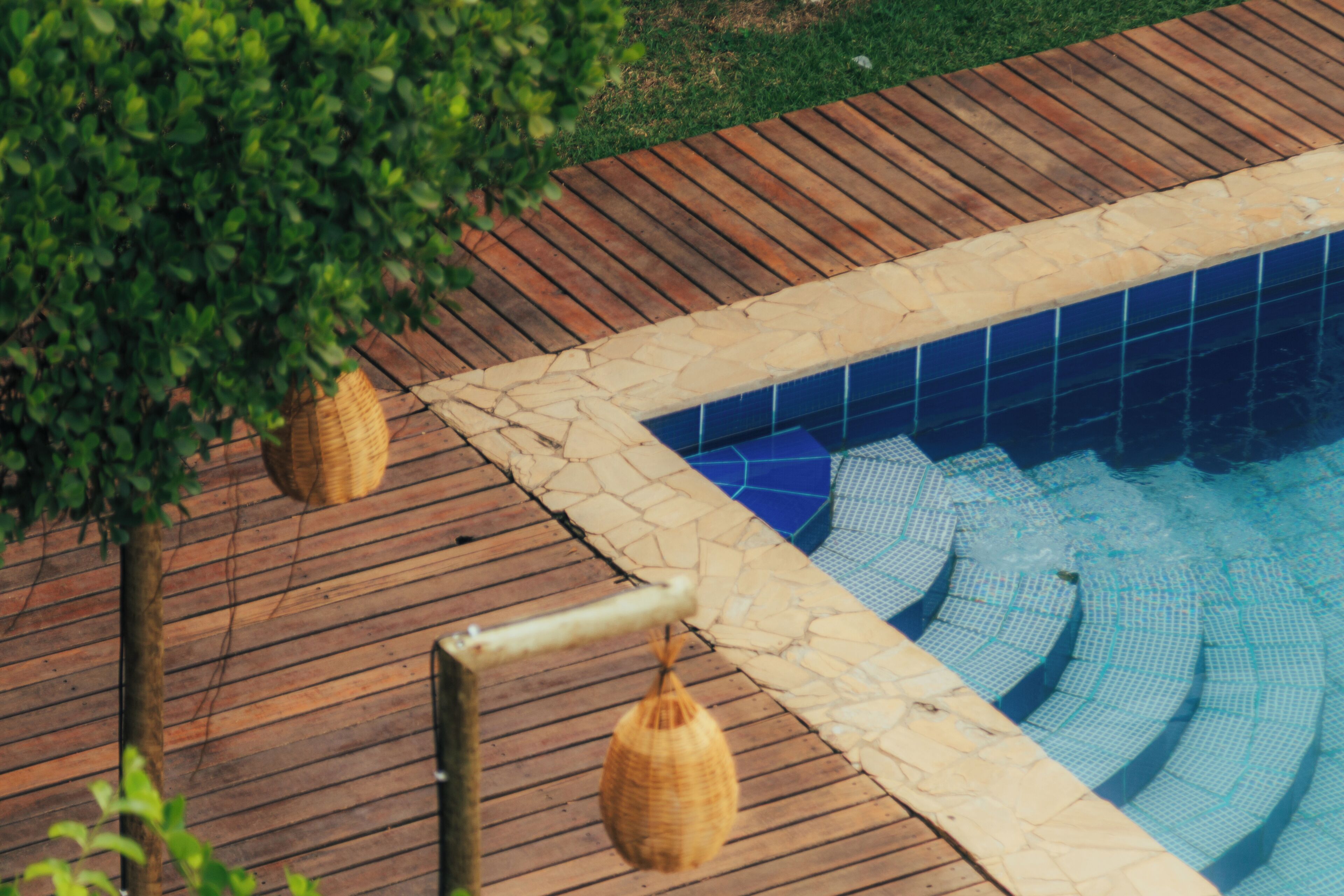 A swimming pool with a wooden deck and stone tiles.