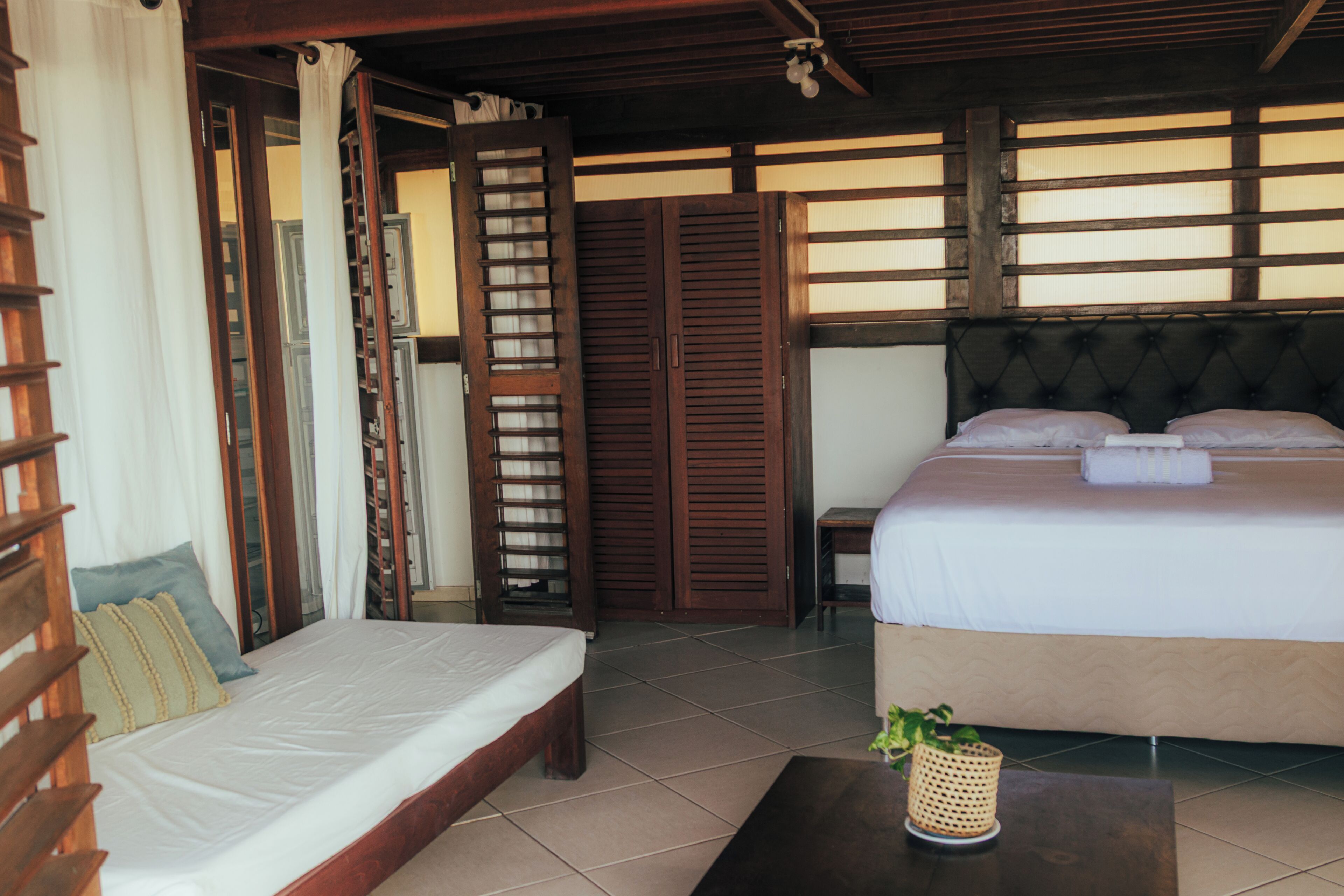 A room with a bed, a desk, a chair, and a small table with a plant.