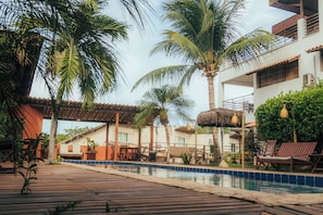 A pool area with lounge chairs, palm trees, and a building with a tiled roof. - Pousada Pipa Panorama (Tibau do Sul)