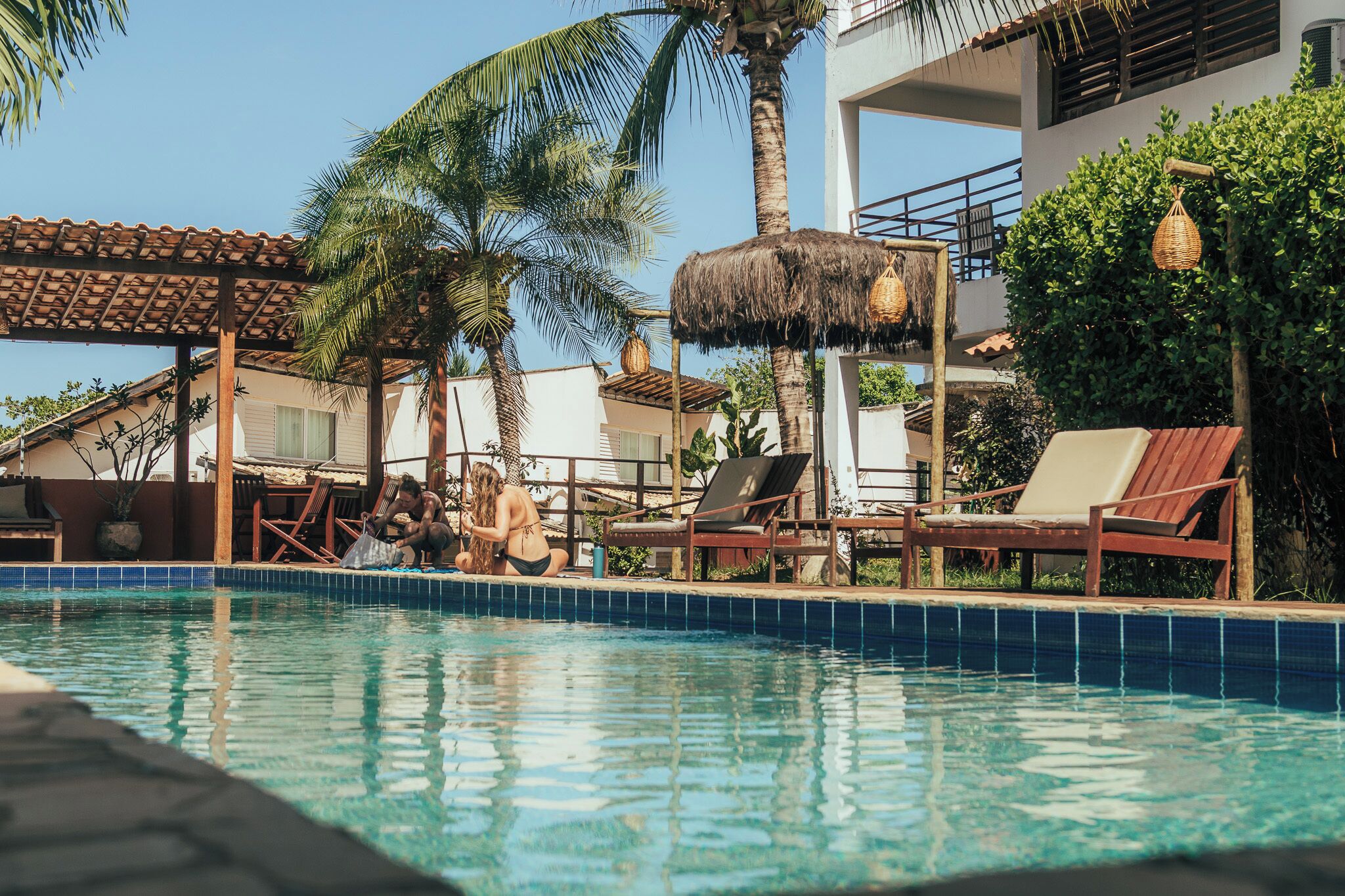 Una piscina con sillones de descanso y una estructura de techo de paja.