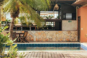 A poolside area with a stone wall, wooden deck, and outdoor seating. - Pipa Panorama Flats&Apartamentos (Tibau do Sul)
