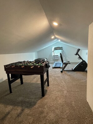 An attic room with a foosball table, a treadmill, and a window.
