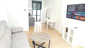 A modern living room with a grey sofa, a round coffee table, and a TV mounted on the wall displaying various channels.