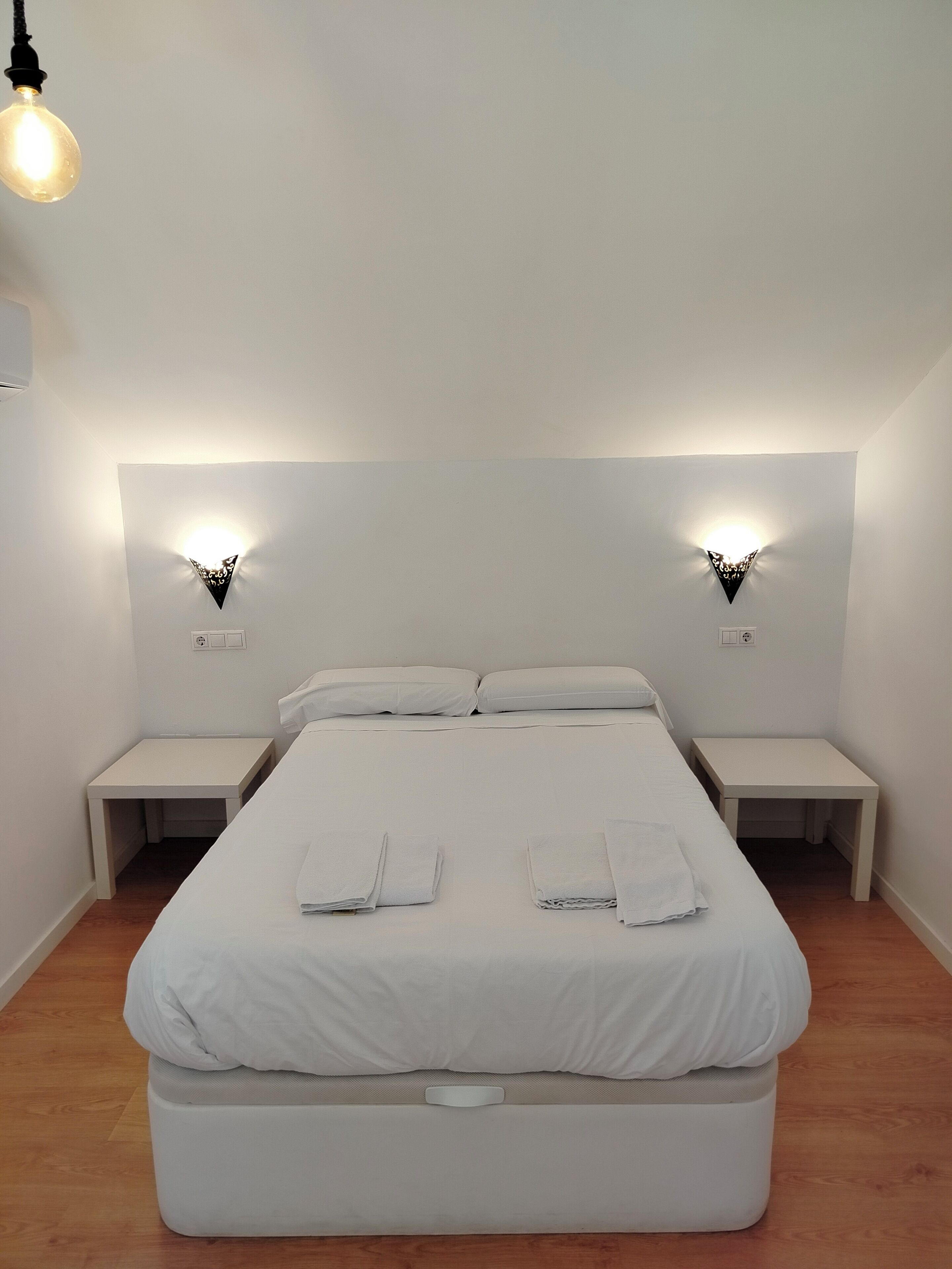 Un dormitorio minimalista con una cama grande, dos mesitas de noche y dos lámparas fijadas a la pared.