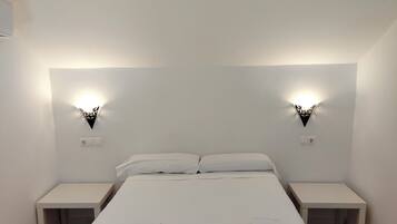 Un dormitorio minimalista con una cama grande, dos mesitas de noche y dos lámparas fijadas a la pared.