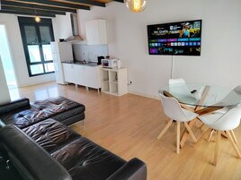 A modern living room with a glass dining table, leather sofa, and a kitchen area with white cabinets and a microwave.