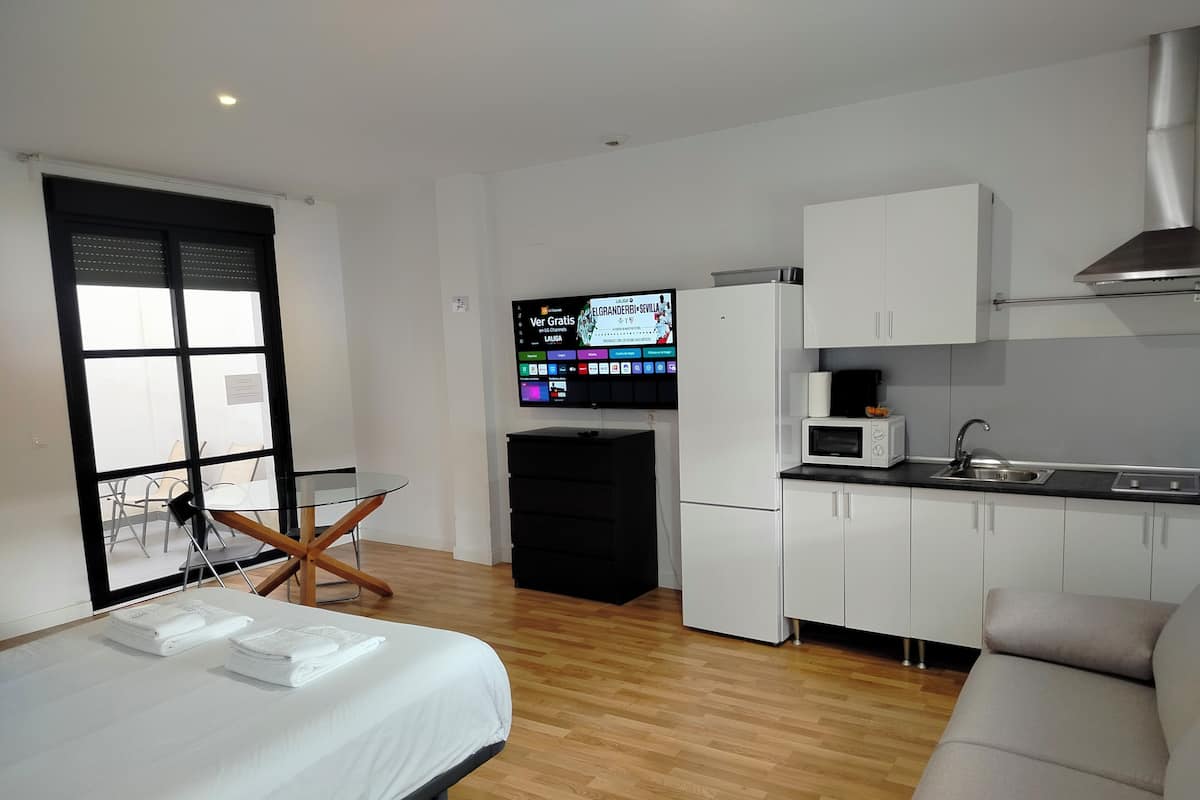 A compact hotel room with a bed, a small dining table, a kitchenette, and a TV.