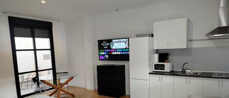 Una habitación de hotel compacta con cama, una pequeña mesa de comedor, una kitchenette y un televisor.