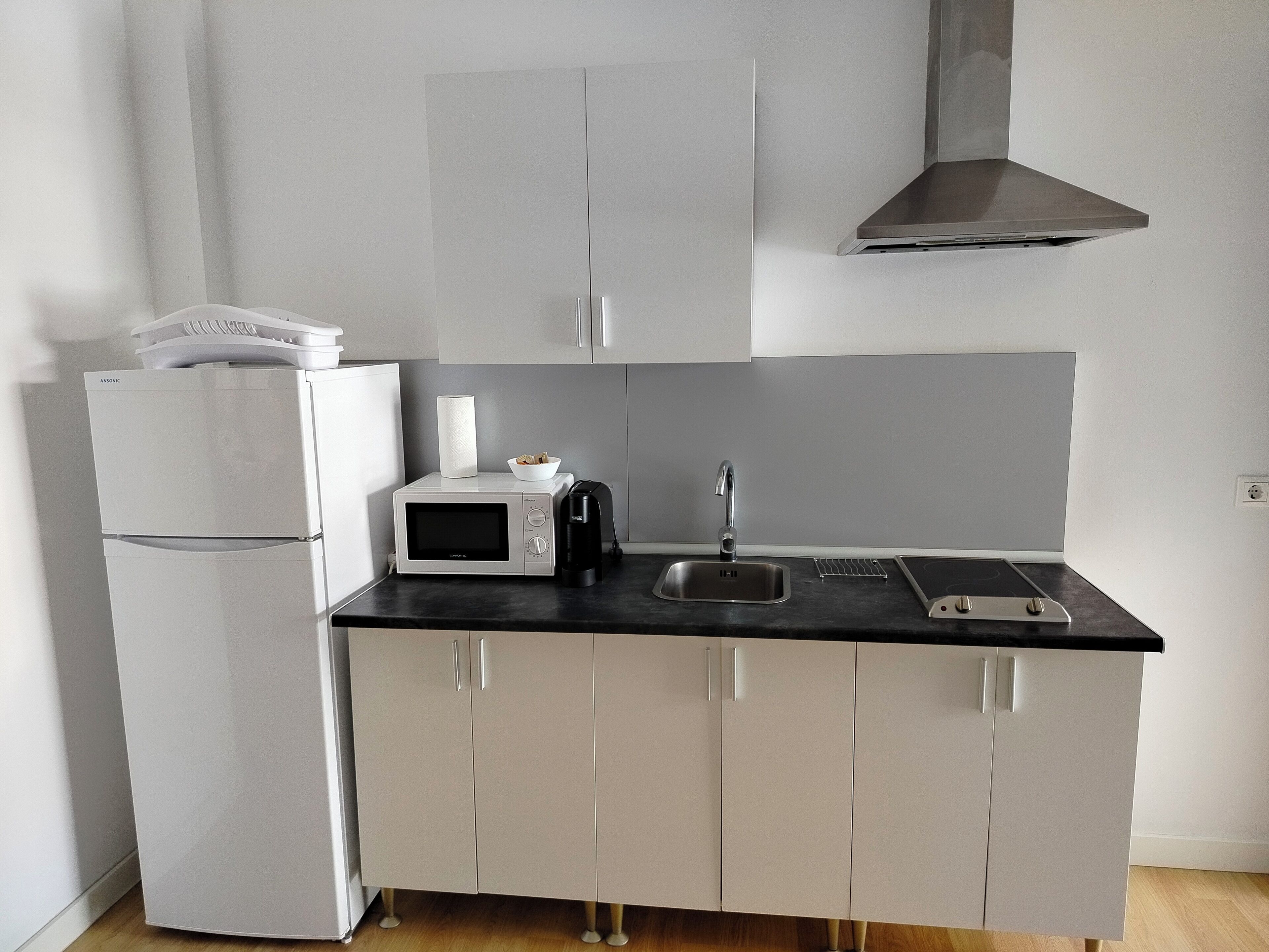 A compact kitchen with a refrigerator, microwave, coffee maker, and a sink.