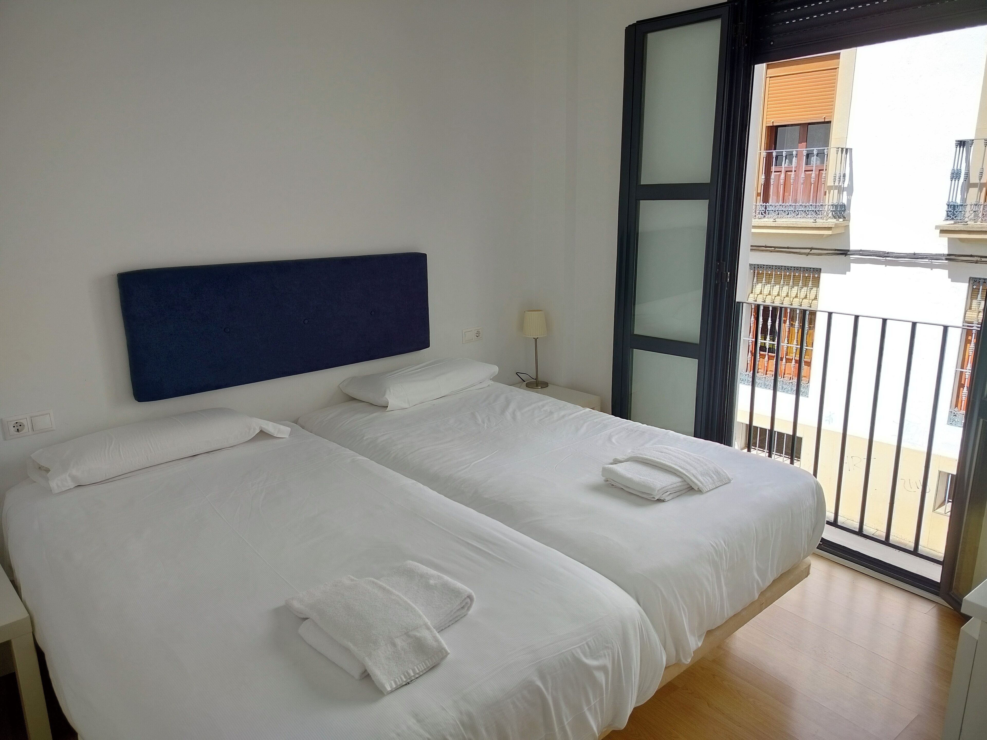 A hotel room with two beds, a large window, and a balcony.