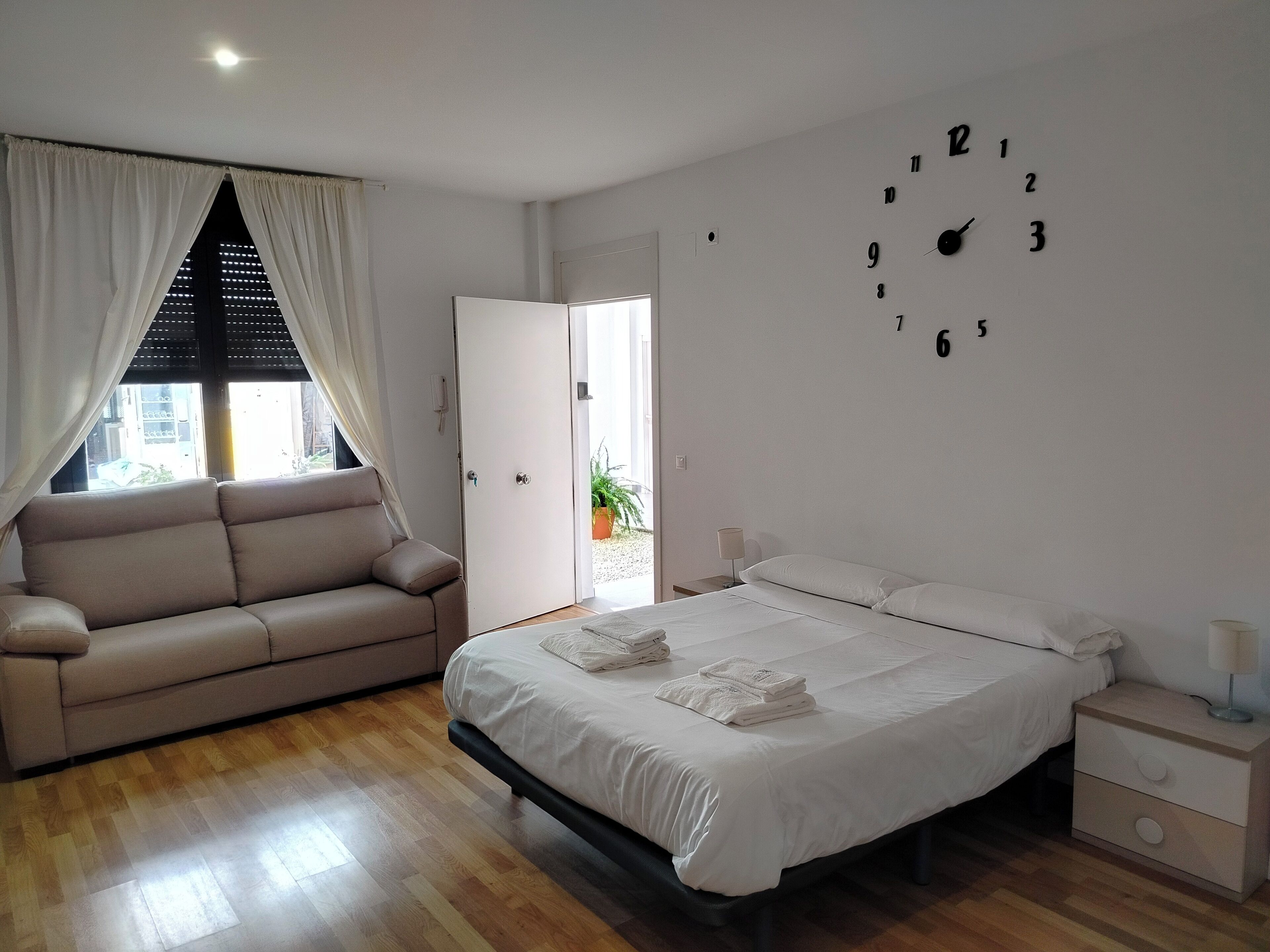 Un dormitorio con cama, sofá, mesita de noche y un reloj de pared.