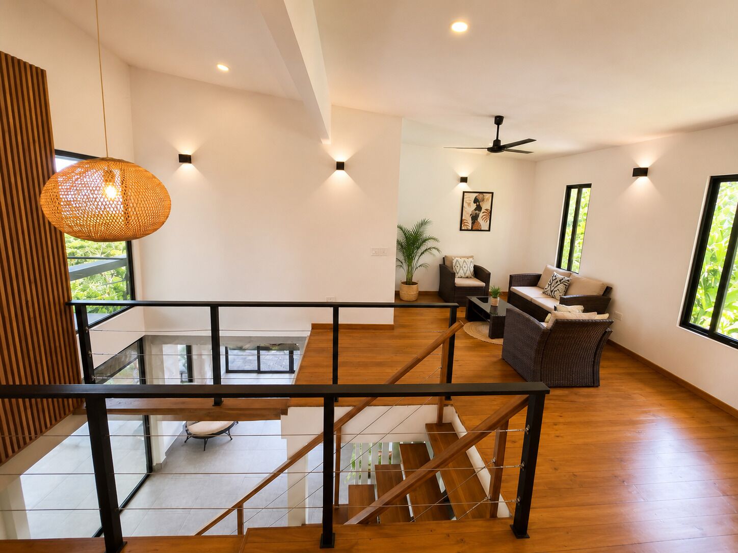 Un intérieur moderne avec un escalier, un coin salon comprenant un canapé et des fauteuils, et un ventilateur de plafond.