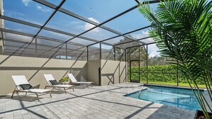 An outdoor pool area with a glass enclosure, three lounge chairs, and a potted plant. - Doppio Luxury Home Themed Magic (Davenport)