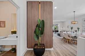 A modern interior with a wooden partition, a potted plant, a dining area with a round table and chairs, and a hanging light fixture.
