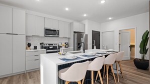 Een moderne keuken met witte kastjes, een centraal eiland met barstoelen, een magnetron, een koelkast en een spoelbak.