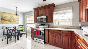 A kitchen with wooden cabinets, a stainless steel oven, and a dining area with chairs and a table. - 9 minutes to Disney Entrance - peaceful single family house (Kissimmee)
