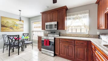 A kitchen with wooden cabinets, a stainless steel oven, and a dining area with chairs and a table.