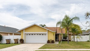 A single-story house with a yellow facade, a white garage, and a small front yard with a palm tree. - 9 minutes to Disney Entrance - peaceful single family house (Kissimmee)