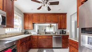 A kitchen with wooden cabinets, stainless steel appliances, a ceiling fan, and a tiled floor. - 9 minutes to Disney Entrance - peaceful single family house (Kissimmee)