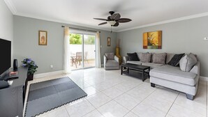 A living room with a grey sofa, a coffee table, a TV, and a ceiling fan. - 9 minutes to Disney Entrance - peaceful single family house (Kissimmee)