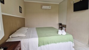 Una camera d'albergo con un letto, una scrivania, una televisione a schermo piatto e un condizionatore d'aria.