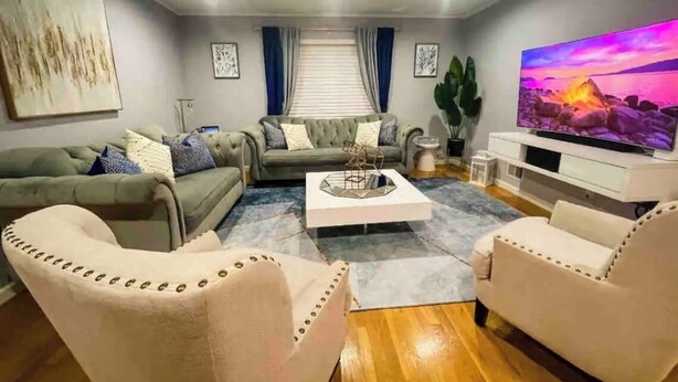 A modern living room with a grey sofa, two armchairs, a coffee table, and a flat-screen TV on a stand. - Modern comfortable 3Beds 2Baths near EWR airport (Elizabeth)