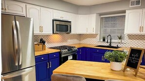 A kitchen with white cabinets, a stainless steel refrigerator, a microwave, a stove, and a wooden dining table with chairs. - Modern comfortable 3Beds 2Baths near EWR airport (Elizabeth)