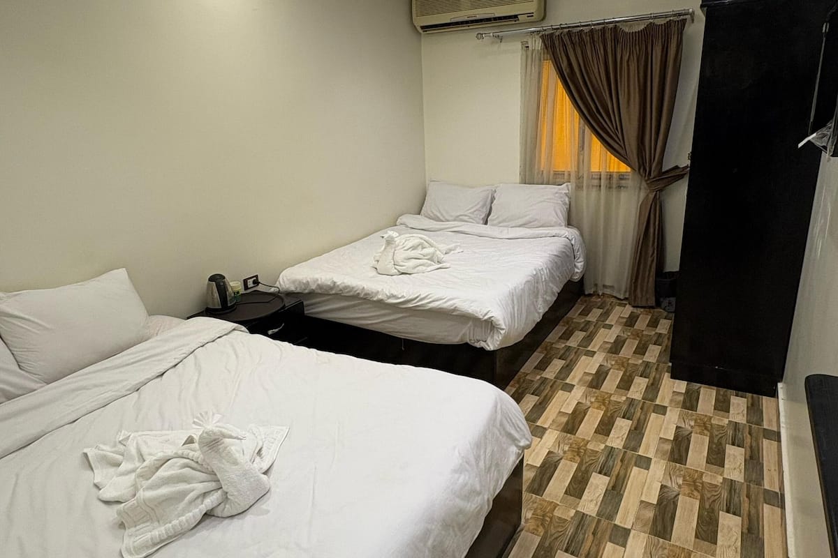 A hotel room with two beds, a wardrobe, an air conditioning unit, and a patterned floor.