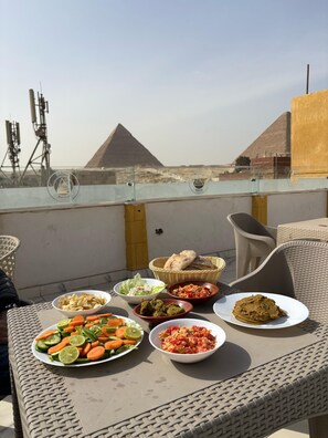 A dining table with various dishes and a view of pyramids in the background. - Amun Ra Pyramids view (Giza)