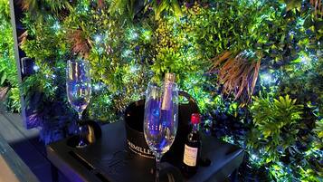 Een bar met twee wijnglazen en een fles wijn op een tafel, omringd door weelderig groen bladwerk.