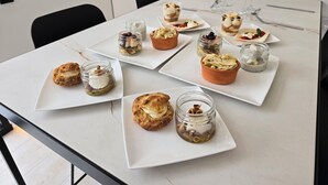 Une table à manger sur laquelle sont disposés divers pâtisseries et desserts, notamment des scones et des tartes aux fruits, présentés sur des assiettes blanches.