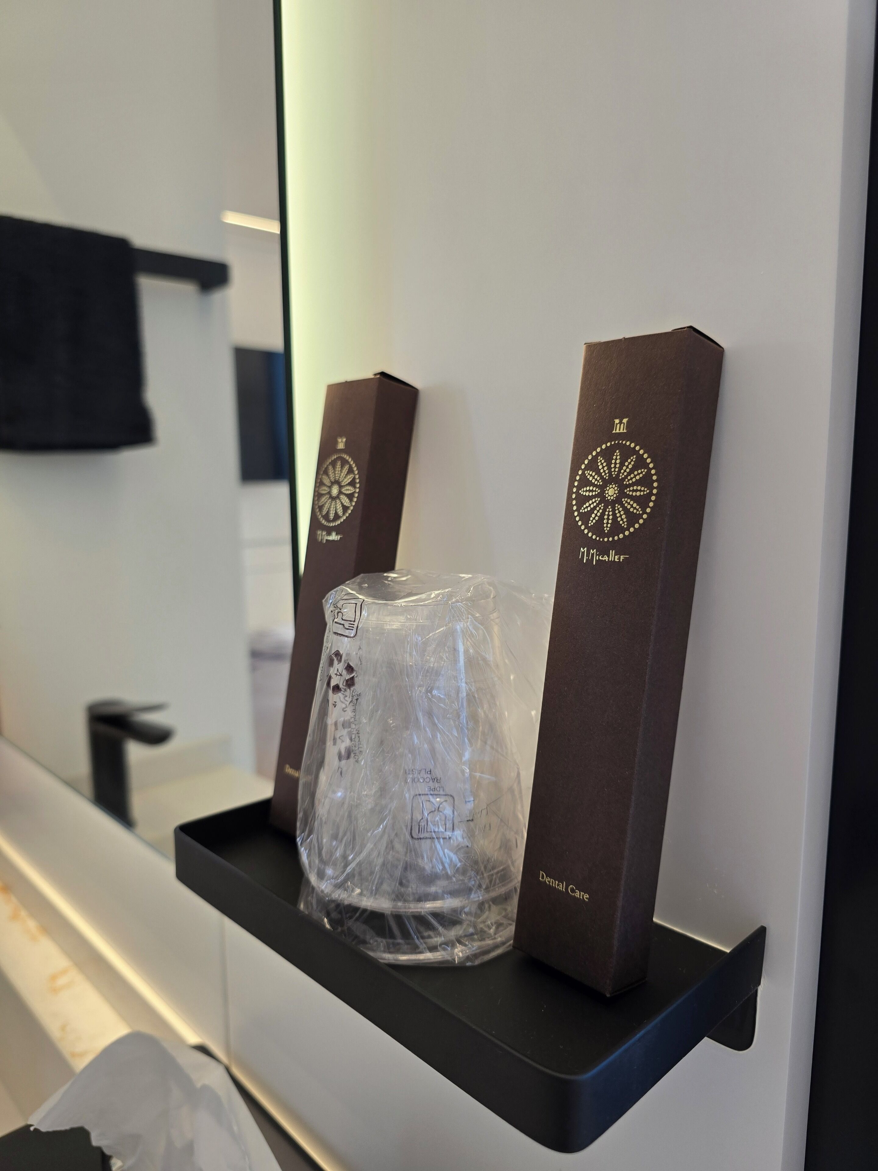 Habitación de hotel con un estante negro que sostiene un objeto envuelto en plástico transparente y dos cajas marrones con diseños dorados.