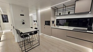 Une cuisine moderne avec un coin repas, dotée d’un parquet en bois clair, de meubles blancs et de tabourets de bar noirs.