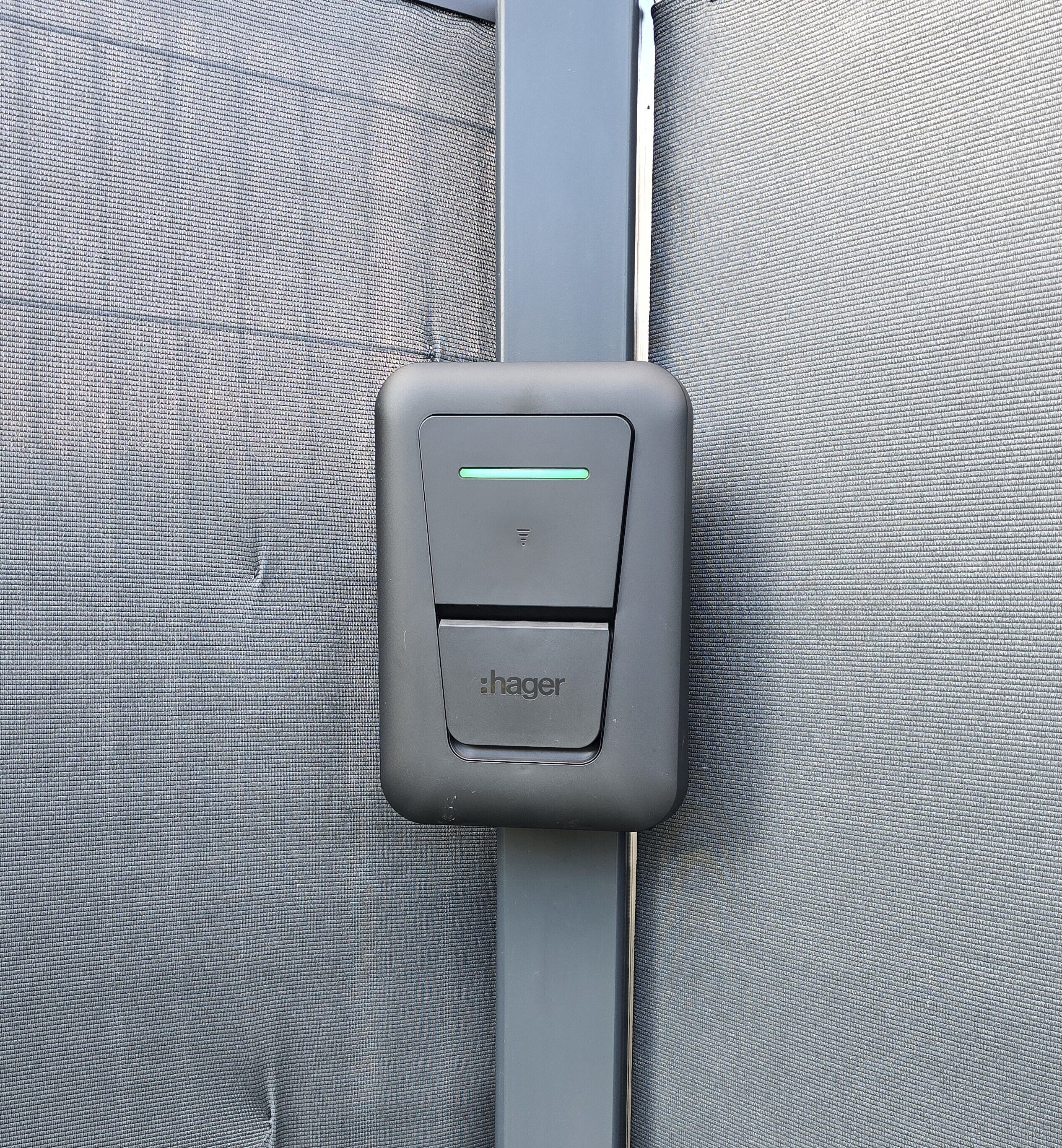 A grey seatbelt buckle with a green light indicator and the brand name 'hager' on a grey fabric surface.