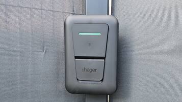 A grey seatbelt buckle with a green light indicator and the brand name 'hager' on a grey fabric surface.