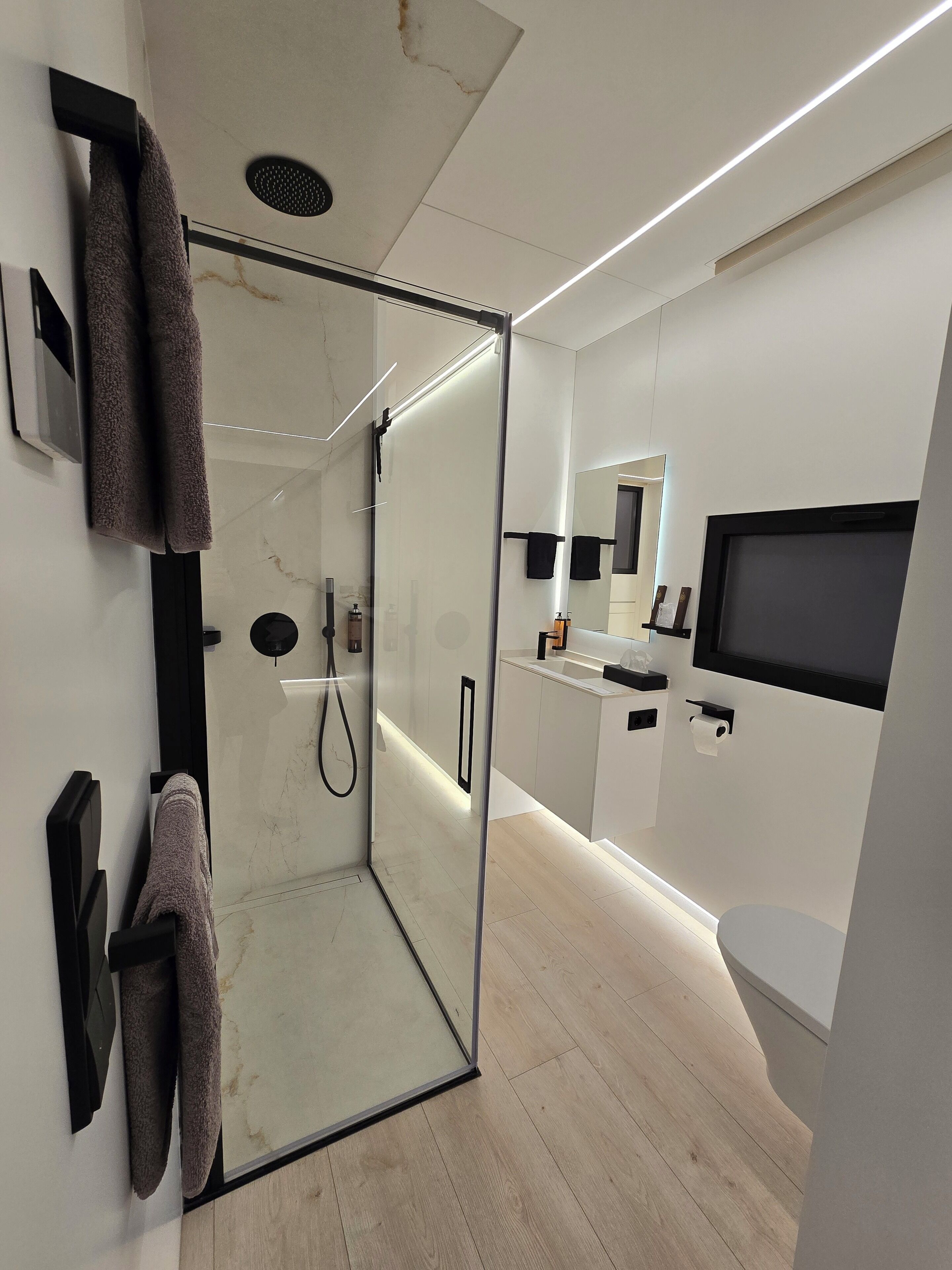 Un baño moderno con ducha de vidrio, inodoro, lavabo y espejo.
