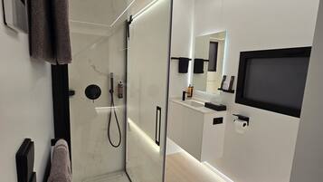 Un baño moderno con ducha de vidrio, inodoro, lavabo y espejo.
