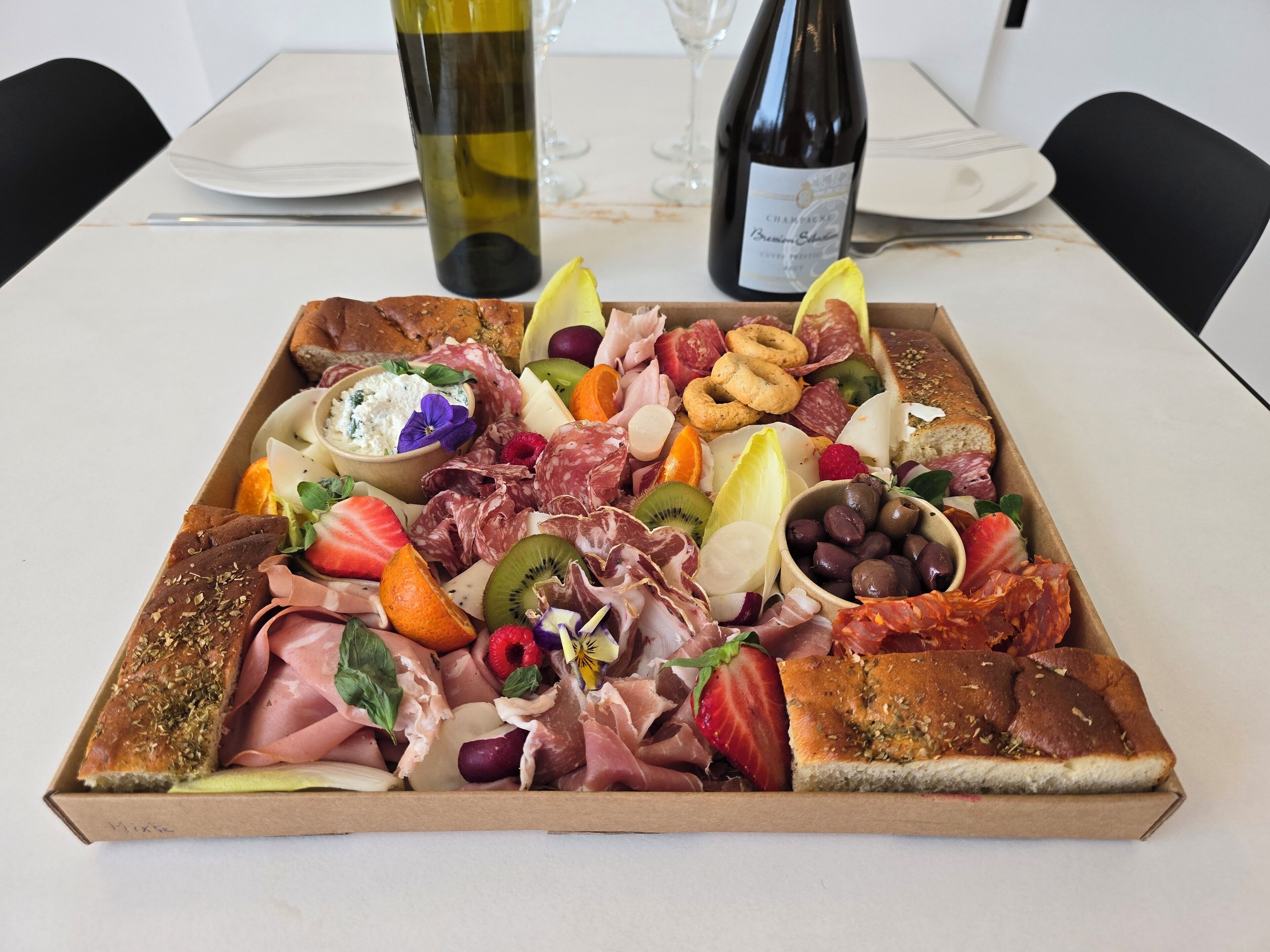 Uma tábua de frios com diversos queijos, carnes, frutas e azeitonas sobre uma mesa.
