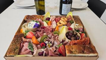 Uma tábua de frios com diversos queijos, carnes, frutas e azeitonas sobre uma mesa.