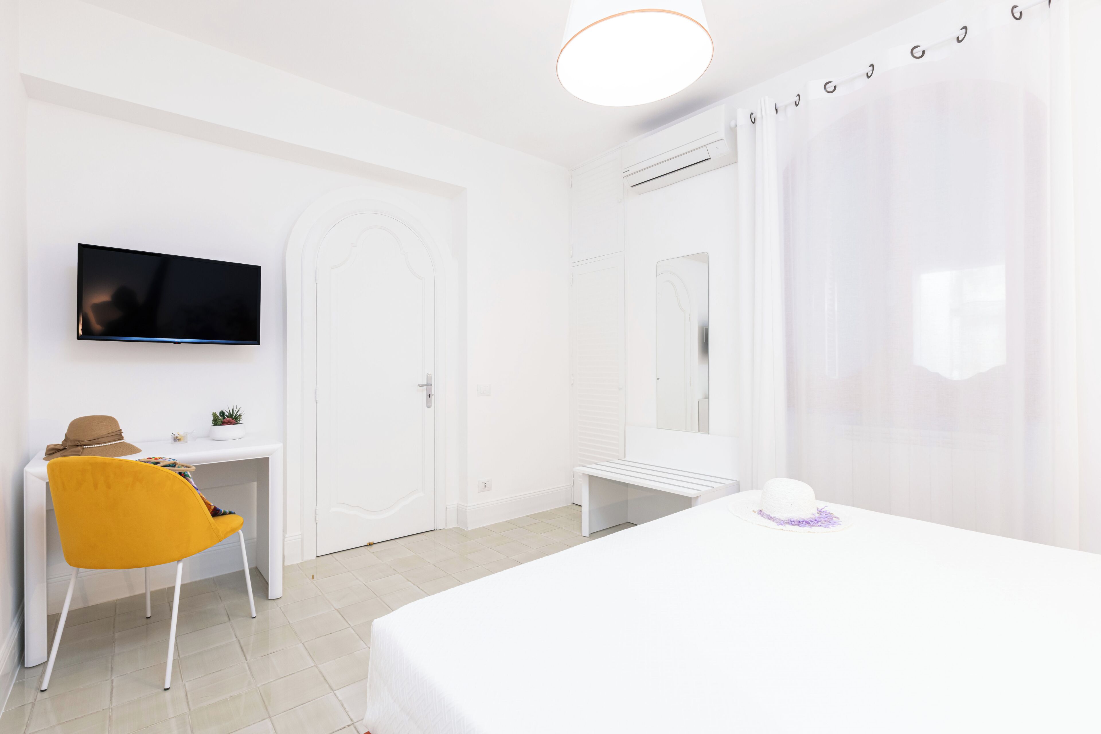 A hotel room with a bed, a desk with a chair, a TV mounted on the wall, and a bathroom with a mirror and shower curtain.