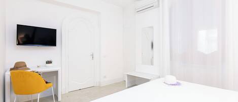 A hotel room with a bed, a desk with a chair, a TV mounted on the wall, and a bathroom with a mirror and shower curtain.