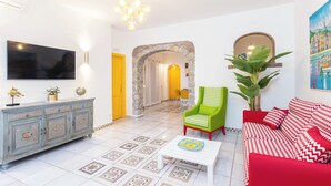A living room with a TV, a sofa, a coffee table, a green armchair, and a red sofa. - YourHome - Villa Magnifica (Positano)
