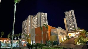 Een modern hotel met meerdere hoge gebouwen, een goed verlichte ingang en een aangelegde omgeving met palmbomen.