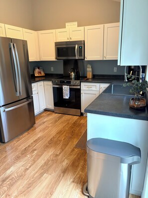 A modern kitchen with stainless steel appliances, white cabinetry, and a wooden floor. - The Central Ranch— minutes to Acadia & Coastal Maine (Ellsworth)