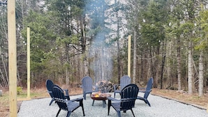 A fire pit surrounded by four Adirondack chairs in a forest setting. - The Central Ranch— minutes to Acadia & Coastal Maine (Ellsworth)